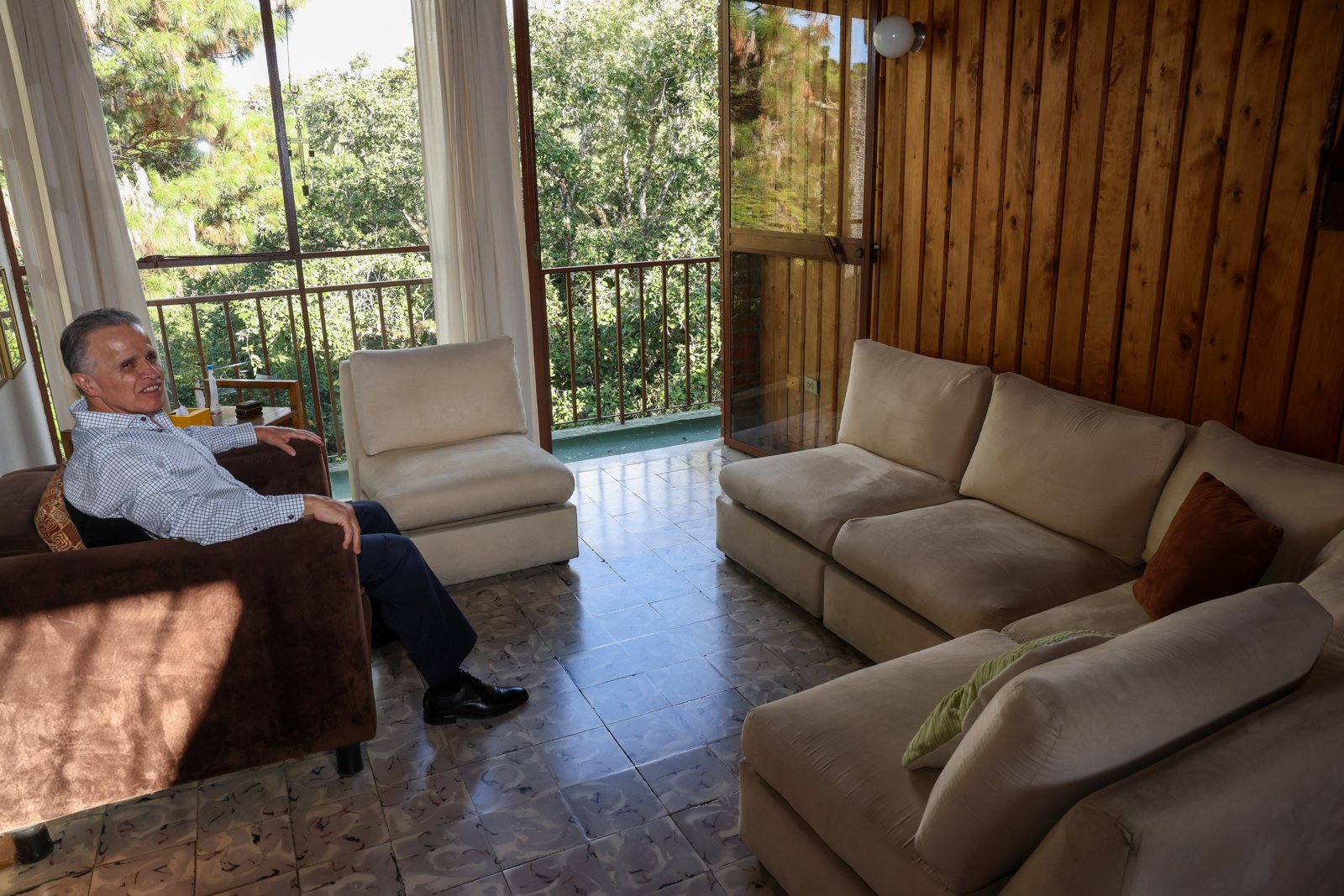 Lic. Fernando Estrada sonriendo, sentado en su sala con vista al balcón